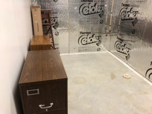 Wood grain filing cabinet in a basement with silver foam insulation walls.