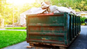 Green 20-yard roll-off dumpster overflowing with renovation debris and cardboard on a residential driveway during a home remodel.