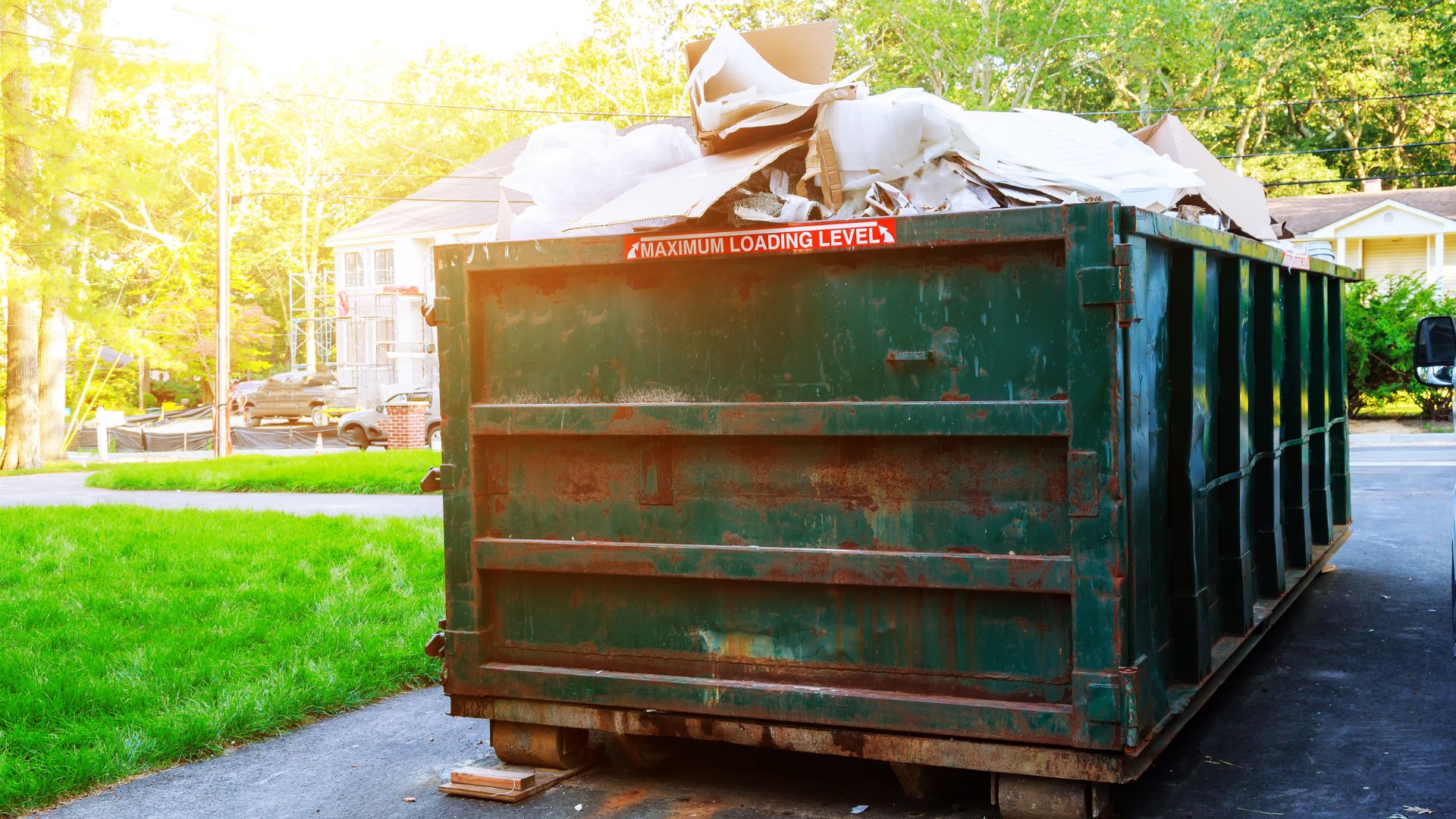 Green 20-yard roll-off dumpster overflowing with renovation debris and cardboard on a residential driveway during a home remodel.